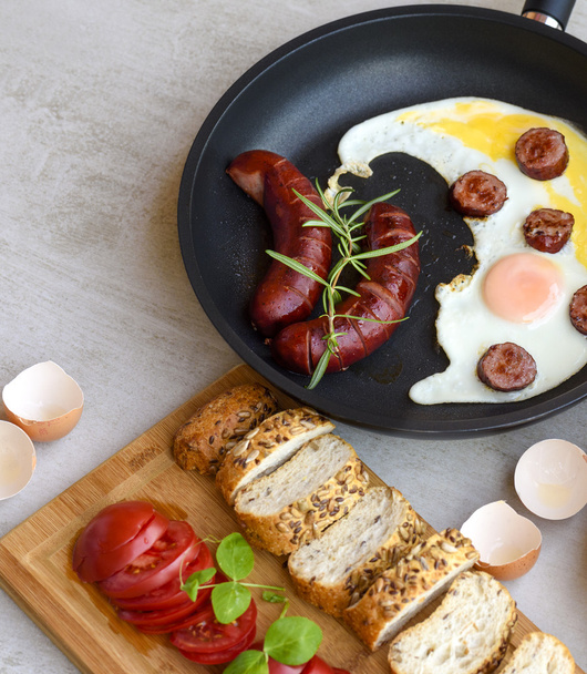 Жареные сосиски и яйца в кастрюле подаются с хлебом, помидорами и яичной скорлупой
 - Фото, изображение
