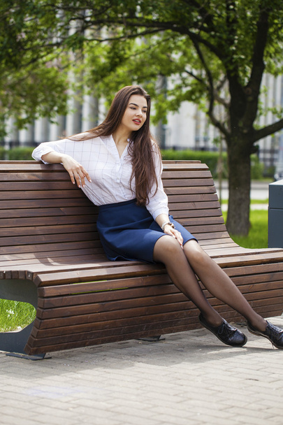 Young beautiful girl sitting on a bench in the summer park - Photo, image