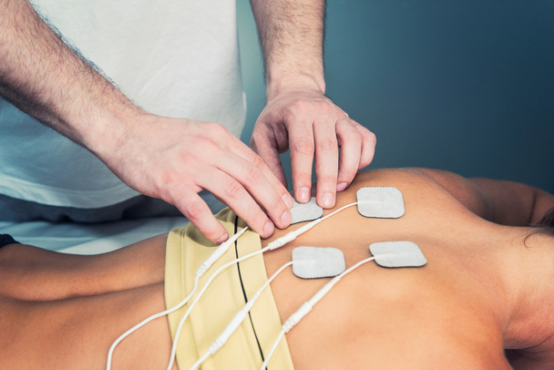 Therapeut positioniert Elektroden am Rücken des Patienten - Foto, Bild