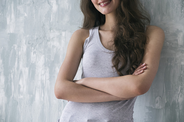Unrecognizable smiling brunette with crossed arms against of grey wall - Fotografie, Obrázek