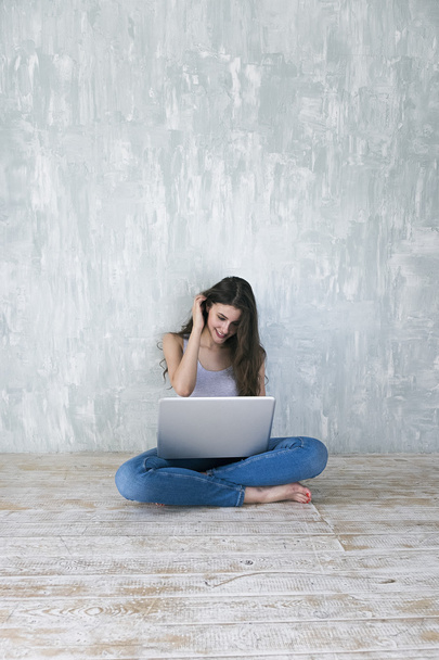 Beautiful brunette using laptop against of cement grunge wall - Zdjęcie, obraz