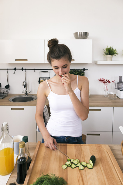 Portrait of brunette eating cut cucumber while cooking - Foto, imagen
