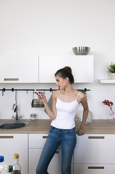 Woman in kitchen using cell phone - Фото, изображение