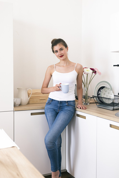 Beautiful brunette with red lips holding cup of coffee in kitchen - Fotoğraf, Görsel