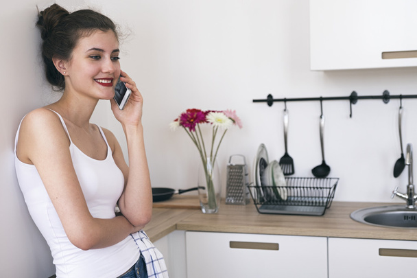 Smiling brunette talking over phone in kitchen - Фото, изображение
