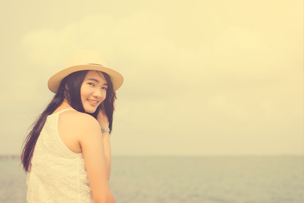 Outdoor summer portrait of young pretty woman looking to the ocean at tropical beach, enjoy her freedom and fresh air, wearing stylish hat and clothes, Vintage filtered image. - Photo, Image