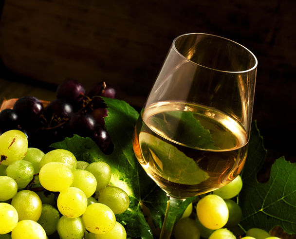 White wine and green grapes in a wicker basket in a wine cellar - Foto, imagen