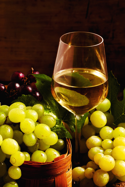 Vino blanco y uvas verdes en una canasta de mimbre en una bodega
 - Foto, Imagen