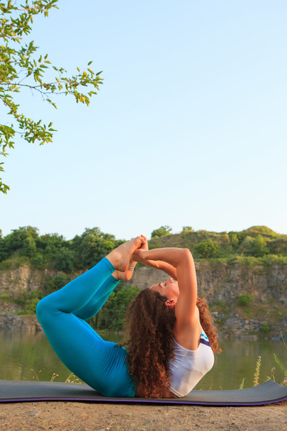 Young woman is practicing yoga near river - 写真・画像