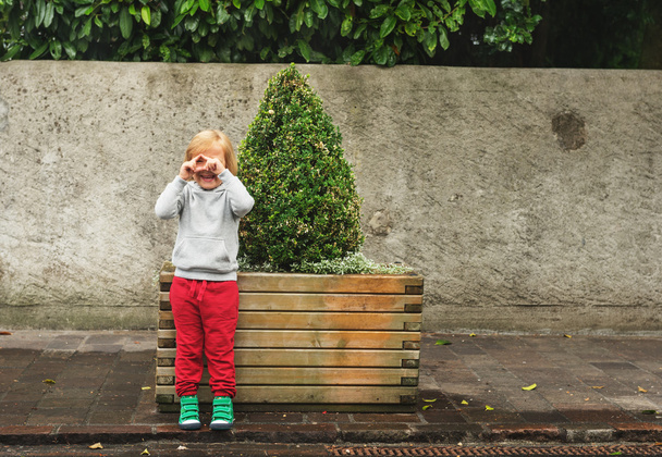 Mode portret van schattig peuter jongen dragen grijs Sweatshirt, rode trainingen en groene schoenen. Kid pretenderen Foto's te nemen met zijn handen - Foto, afbeelding