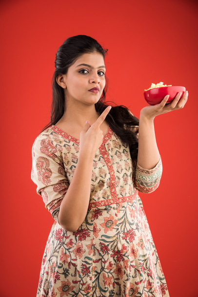 ινδική νεαρής και όμορφης κοπέλας, τρώγοντας ποπ κορν, ασιατικό κορίτσι απολαμβάνει ποπ κορν ή ποπ-κορν, απομονώνονται σε κόκκινο φόντο - Φωτογραφία, εικόνα