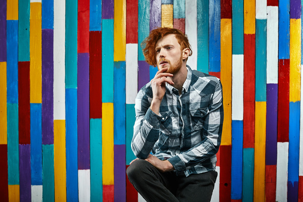 young thoughtful redhead bearded man in plaid shirt on colourful - Foto, afbeelding