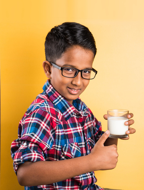 indian boy with a glass of milk, indian kid drinking milk, indian boy drinking milk,asian boy and milk, closeup portrait on yellow background - Photo, Image