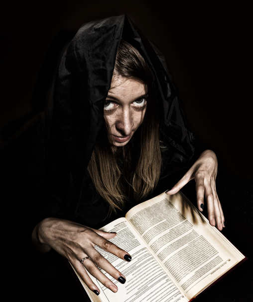 pretty witch casts spells from thick ancient book by candlelight on a dark background - Photo, Image