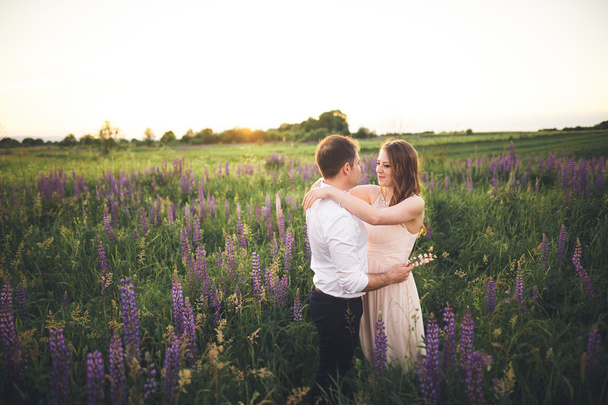 Emotional beautiful bride hugging newlywed groom from behind sunset at a field closeup - Фото, изображение