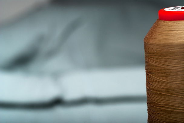 Detail einer Nadel mit Faden in der Garnrolle des Arbeitszimmers und natürlichem Stoff. Arbeitstisch eines Schneiders. Nähtextilien oder Stoffe. geringe Schärfentiefe. Fokus auf Rolle des Fadens - Foto, Bild