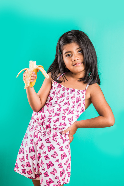 Intialainen tyttö syö banaania, 4-vuotias aasialainen tyttö syö banaania, tyttö banaani, pieni tyttö tai pieni tyttö syö banaania, eristetty vihreällä taustalla
 - Valokuva, kuva