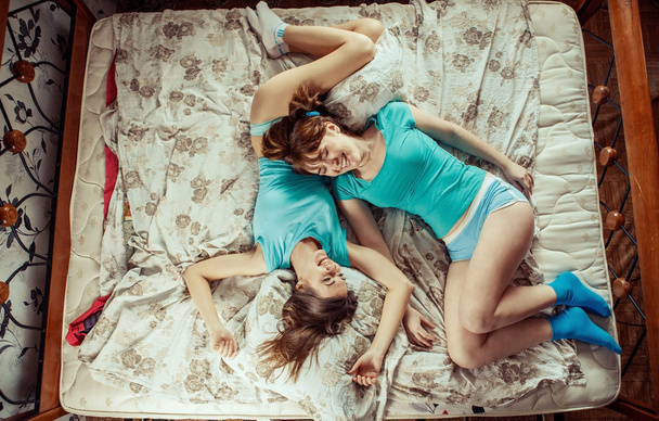 Two girls in blue t-shirts laughing on the bed. - Фото, зображення