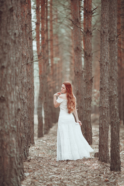 Ginger girl in white dress walking in pine forest. - Zdjęcie, obraz