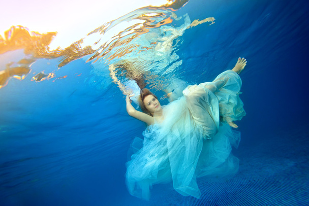 Girl dancing underwater in a white wedding dress against a blue background - Foto, afbeelding