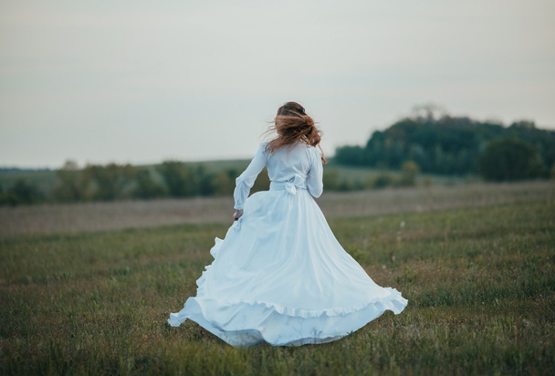 Girl in white vintage dress walking through the spring field. - Photo, Image