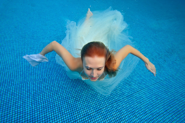 The bride swims underwater in a white wedding dress against a blue background - Fotoğraf, Görsel