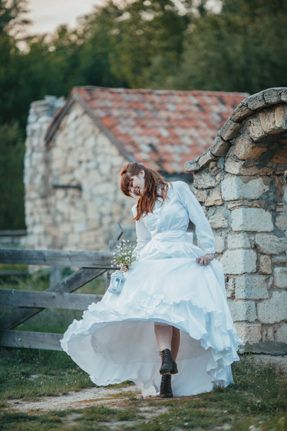 Beautiful girl in white vintage dress walking near ancient stone house. Vintage bridal concept - Foto, afbeelding