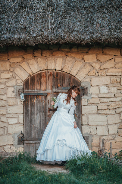 Beautiful girl in white vintage dress walking near ancient stone house. Vintage bridal concept - Foto, Imagem