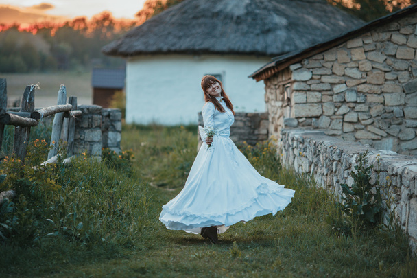 Beautiful girl in white vintage dress walking near ancient stone house. Vintage bridal concept - Photo, Image