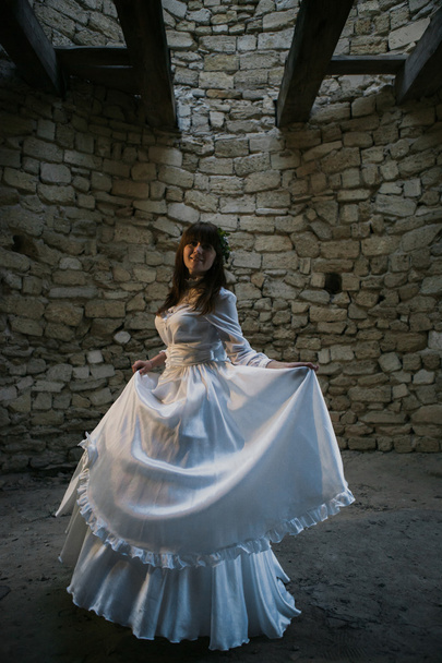 Beautiful girl in white vintage dress walking near ancient stone house. Vintage bridal concept - Photo, Image