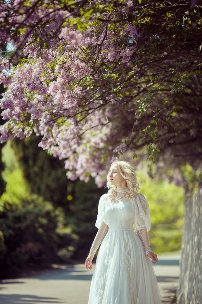 Beautiful blonde woman in blooming lilac garden. Vintage bride concept - Фото, изображение