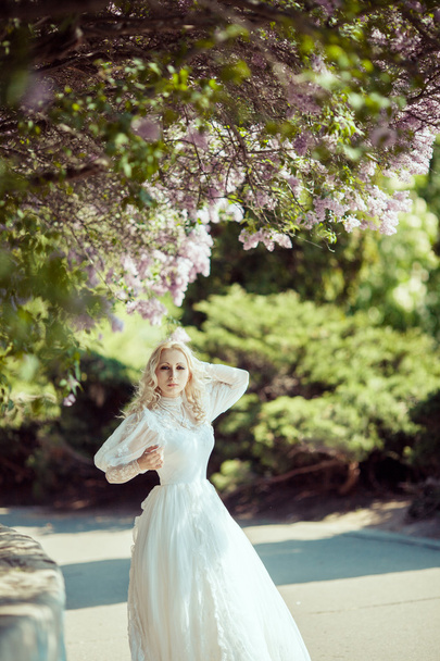 Beautiful blonde woman in blooming lilac garden. Vintage bride concept - Fotografie, Obrázek