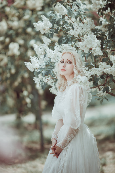 Beautiful blonde woman in blooming lilac garden. Vintage bride c - Valokuva, kuva