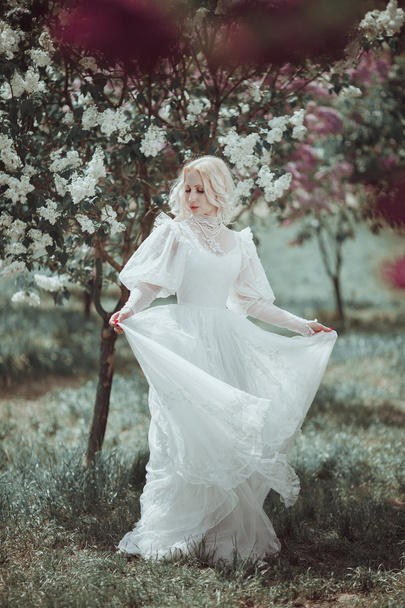 Beautiful blonde woman in blooming lilac garden. Vintage bride c - 写真・画像