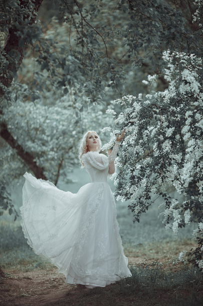 Beautiful blonde woman in blooming lilac garden. Vintage bride c - 写真・画像