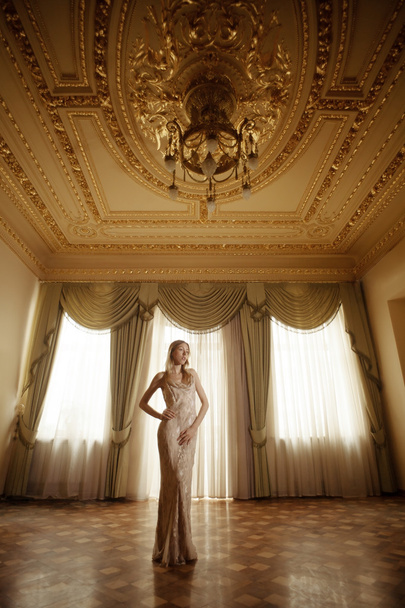 Beautiful girl in long dress flying in golden baroque interior. - Fotó, kép