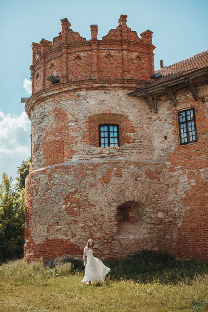 Beautiful young girl in white vintage dress walking near ancient castle. - Photo, Image