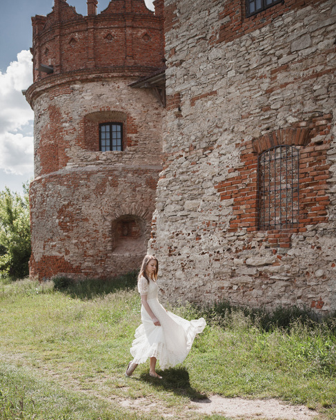Beautiful young girl in white vintage dress walking near ancient castle. - Photo, Image