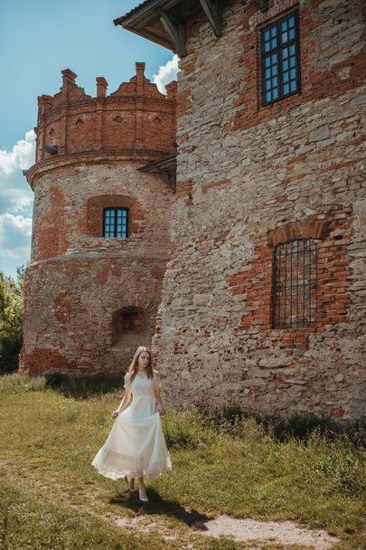 Beautiful young girl in white vintage dress walking near ancient castle. - Foto, afbeelding