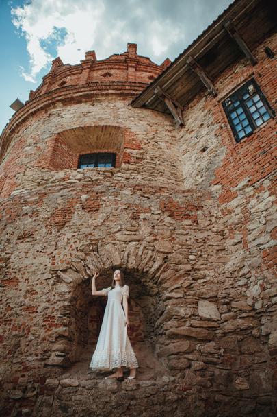 Beautiful young girl in white vintage dress walking near ancient castle. - Foto, Bild