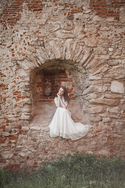 Beautiful young girl in white vintage dress walking near ancient castle. - Fotoğraf, Görsel