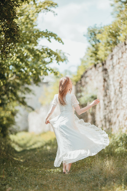 Beautiful young girl in white vintage dress walking near ancient castle. - Zdjęcie, obraz