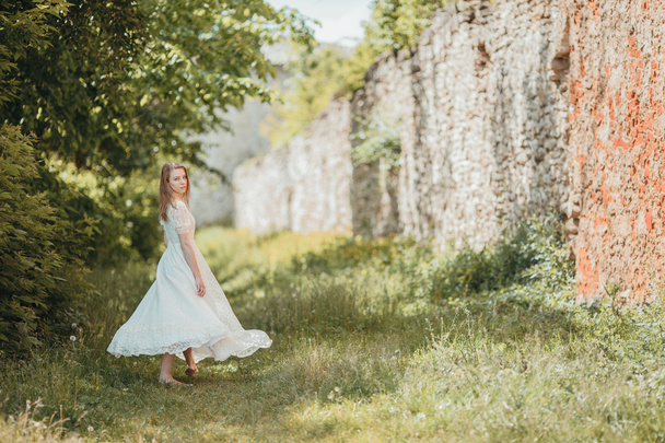 Beautiful young girl in white vintage dress walking near ancient castle. - Foto, afbeelding