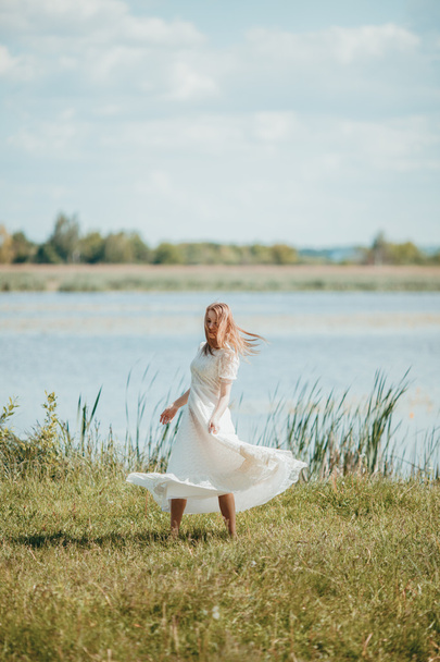 Beautiful young lady in white vintage dress walking near the river in the sun. - Fotografie, Obrázek