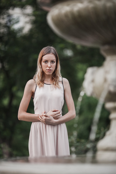 Beautiful young girl in fashionable pink dress standing near vintage stone fountain. - Foto, immagini