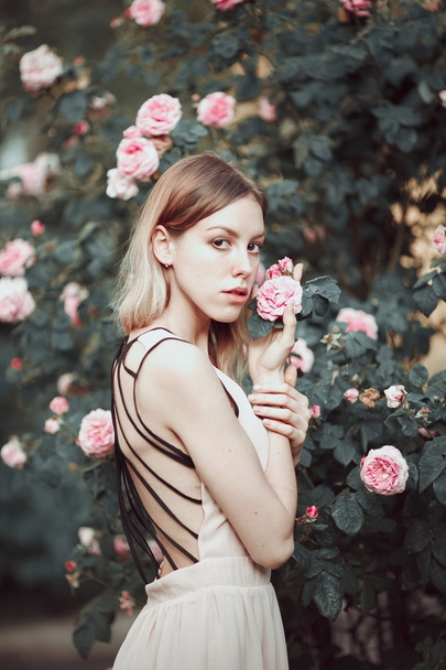 Beautiful young girl in fashionable pink dress smelling roses. Fairytale. Fashion. Fantasy - Zdjęcie, obraz