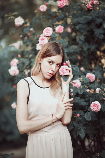 Beautiful young girl in fashionable pink dress smelling roses. Fairytale. Fashion. Fantasy - Photo, Image