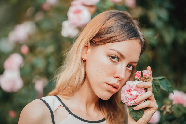 Beautiful young girl in fashionable pink dress smelling roses. Fairytale. Fashion. Fantasy - Foto, afbeelding