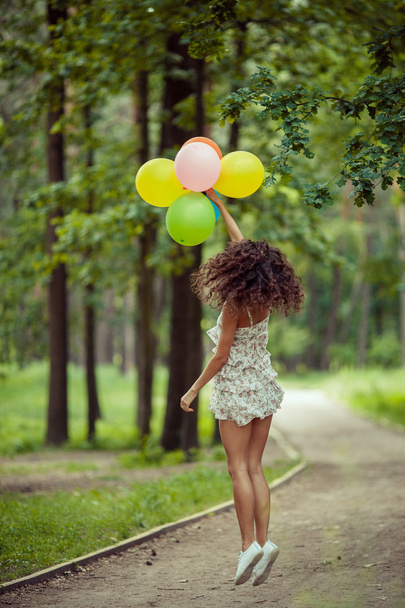 Szép fiatal lány szórakozás a nyári parkban színes lufik ünnepe. Boldog mosollyal ugrás koncepció - Fotó, kép