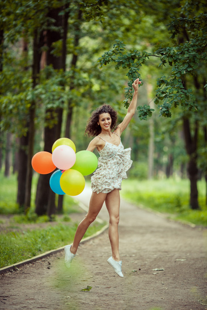Mooi jong meisje, plezier in het park van de zomer met gekleurde ballonnen. Happy glimlach sprong concept - Foto, afbeelding